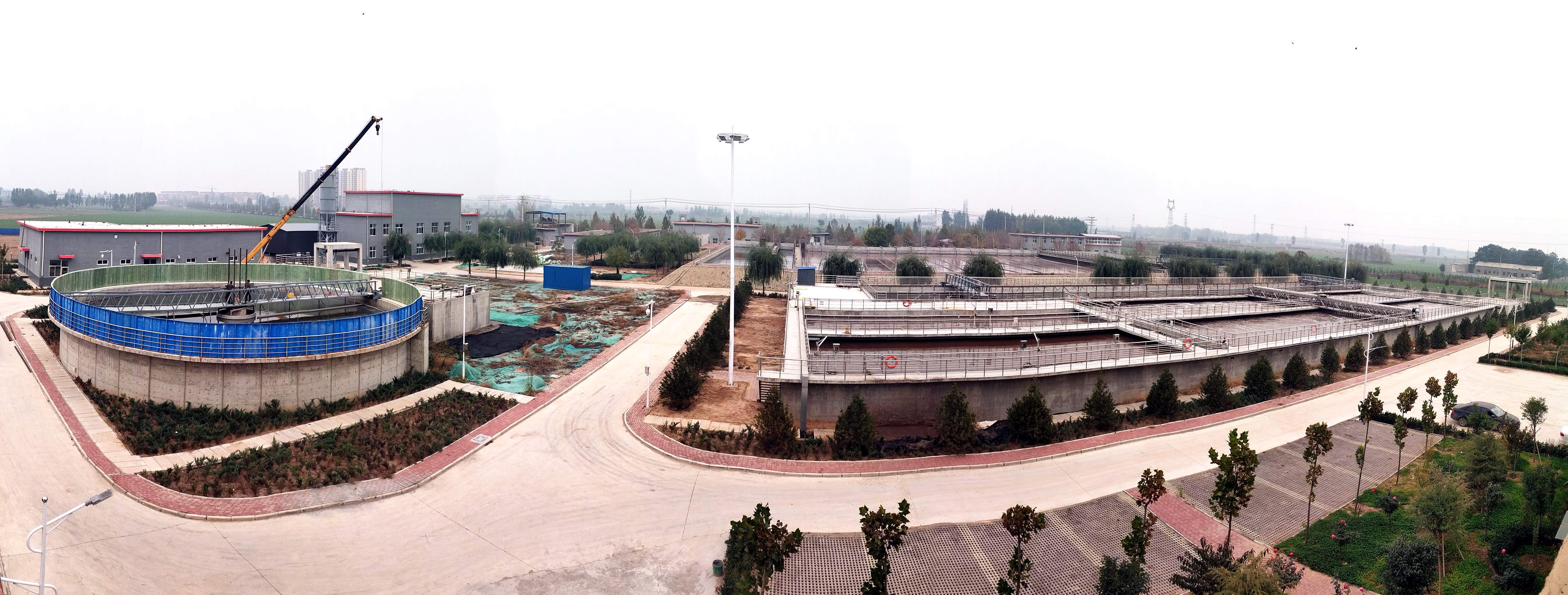 俯瞰工业处理设施，圆形与矩形水池整齐排列，道路与绿化带穿插其间，呈现市政工程的规整布局